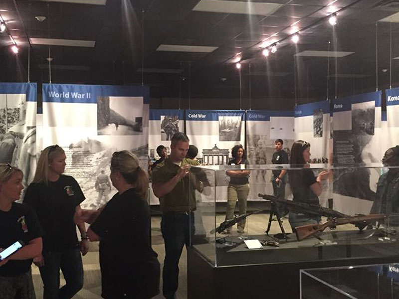 10 people standing inside a museum room looking at several exhibits.